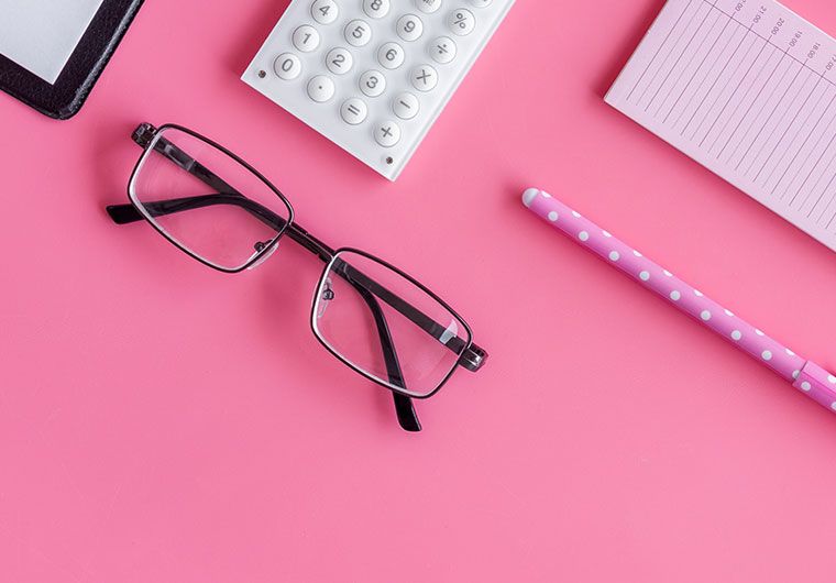 A surface with a pair of glasses, a calculator, and writing tools