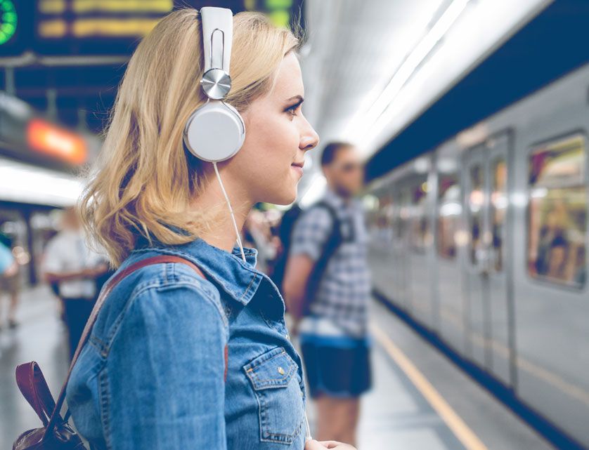 A woman wearing headphones waiting to board a subway