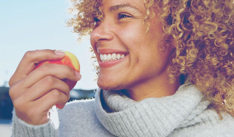 A woman smiling and holding an apple