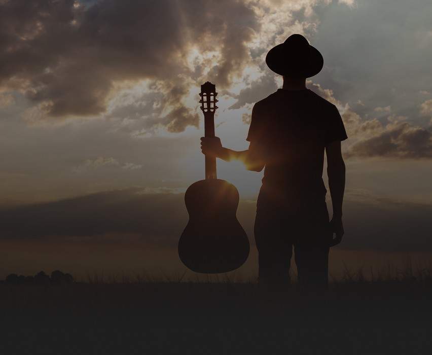 A silhouetted man holding an acoustic guitar