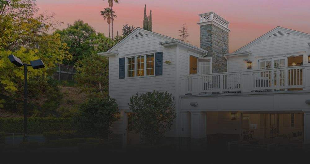 A white house with a pink sunrise behind it