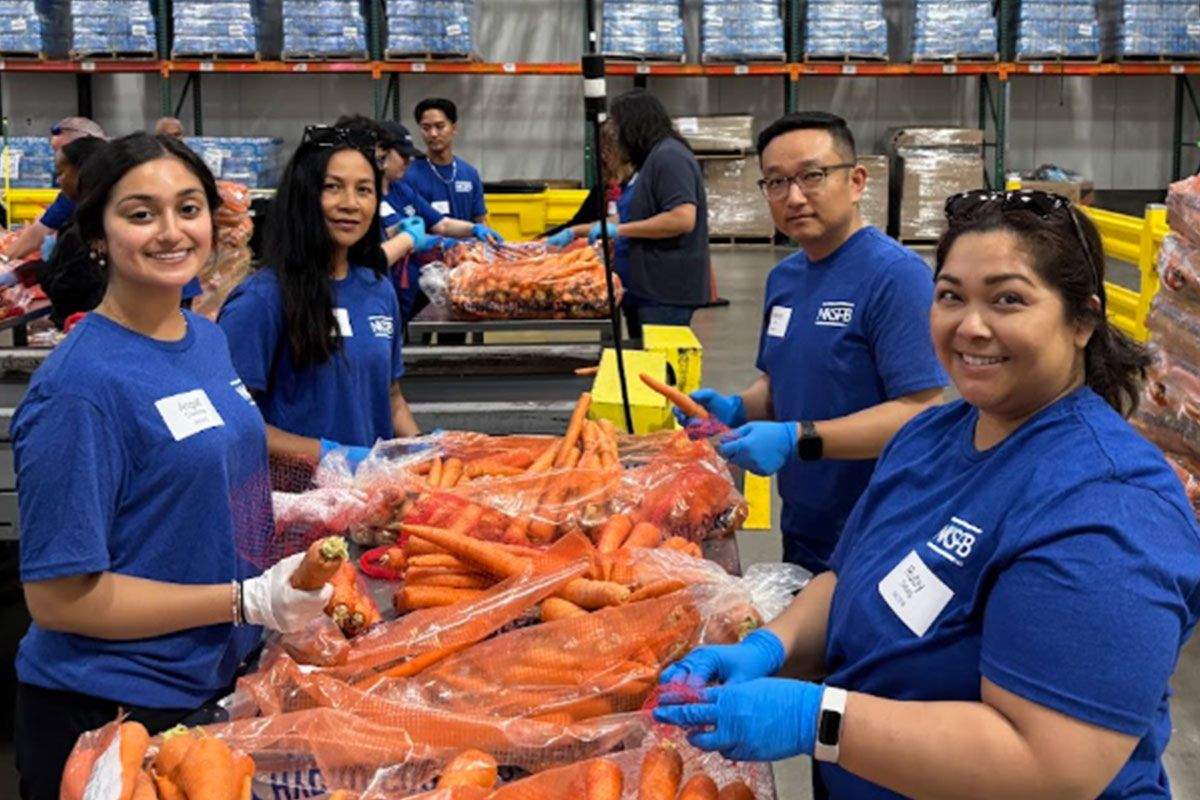 Four smiling individuals in blue shirts holding fresh carrots.