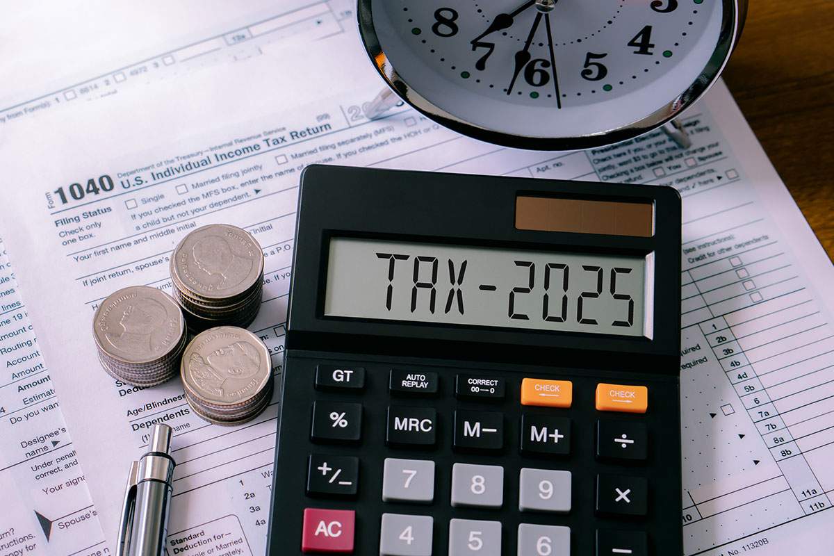 Taxes and a calculator placed on a wooden desk, with papers and a pen nearby